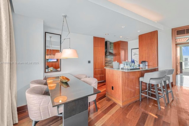 kitchen featuring kitchen peninsula, a breakfast bar area, dark wood-type flooring, and wall chimney range hood