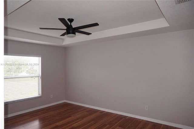 unfurnished room with dark hardwood / wood-style flooring, a tray ceiling, and ceiling fan