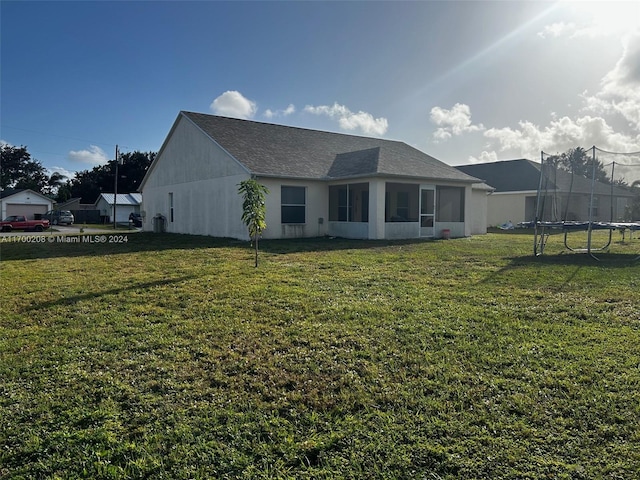 back of property featuring a yard, a trampoline, and a sunroom