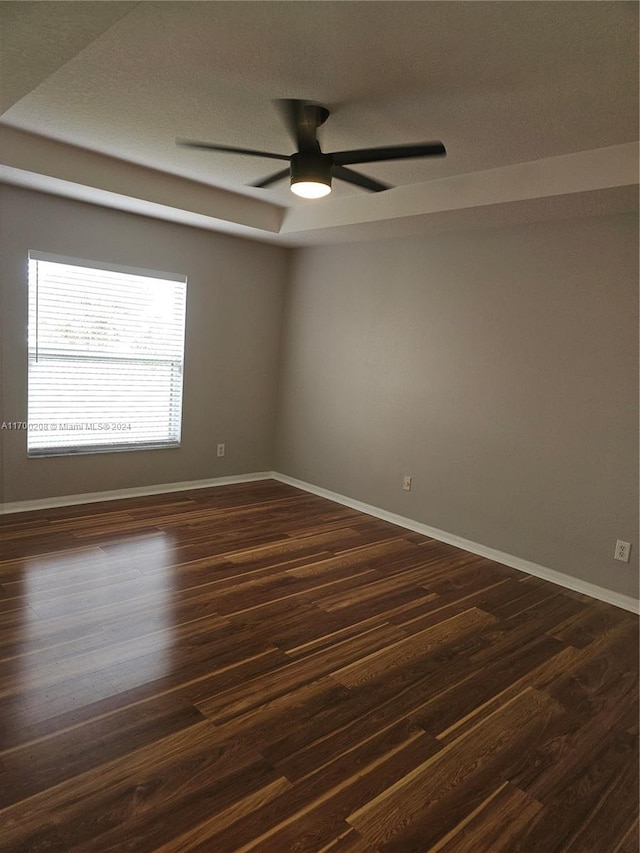 unfurnished room featuring a raised ceiling, ceiling fan, and dark hardwood / wood-style flooring