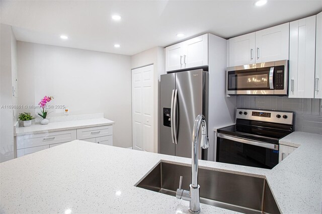 kitchen featuring white cabinets, appliances with stainless steel finishes, light stone counters, and sink