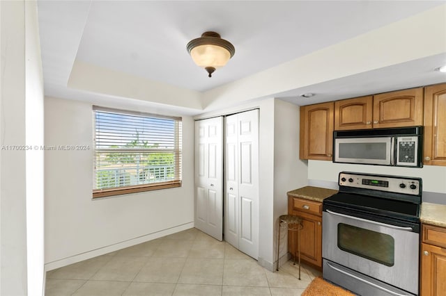 kitchen featuring light tile patterned flooring, appliances with stainless steel finishes, and dark stone countertops