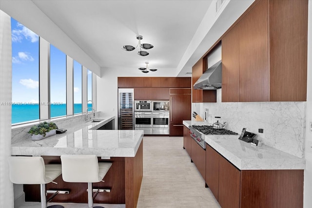 kitchen with a water view, sink, wall chimney exhaust hood, kitchen peninsula, and a breakfast bar area