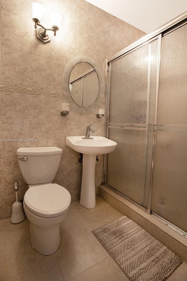 bathroom with toilet, tile patterned floors, a sink, a shower stall, and tile walls