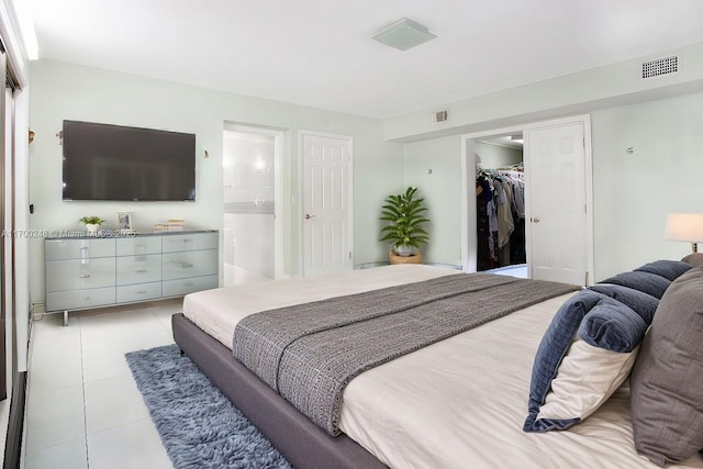 bedroom with light tile patterned floors, connected bathroom, visible vents, and a walk in closet