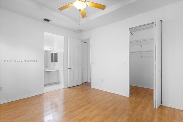 unfurnished bedroom with ensuite bath, ceiling fan, a spacious closet, a closet, and light wood-type flooring