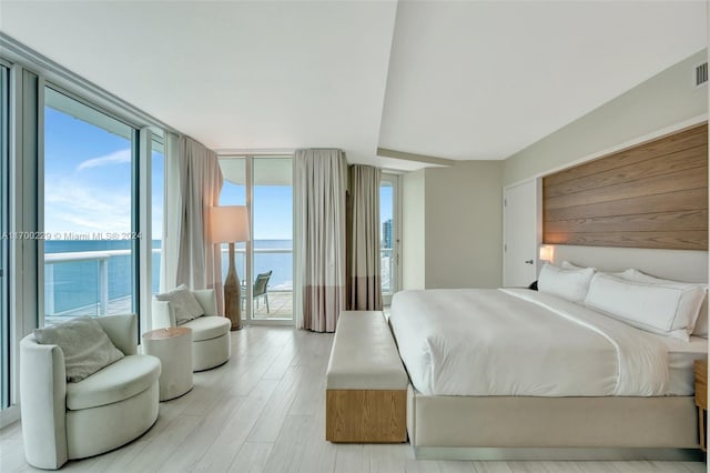 bedroom with access to outside, a water view, light hardwood / wood-style flooring, and a wall of windows