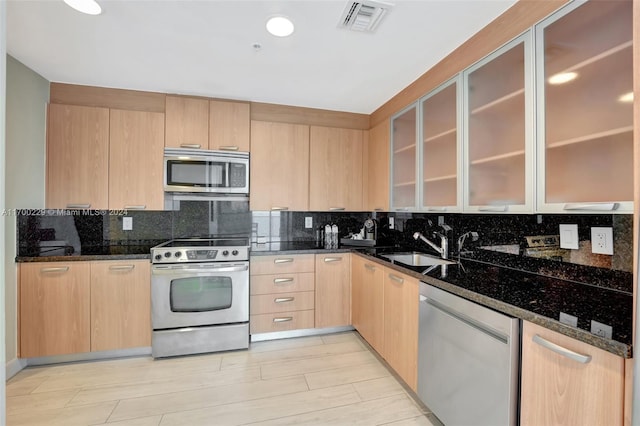 kitchen with decorative backsplash, light brown cabinetry, stainless steel appliances, and dark stone countertops