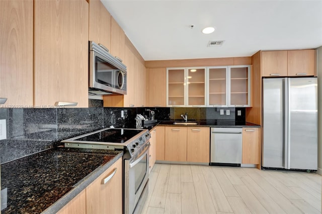 kitchen with dark stone counters, light brown cabinetry, tasteful backsplash, appliances with stainless steel finishes, and light hardwood / wood-style floors