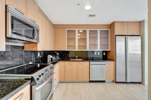 kitchen with light brown cabinets, light hardwood / wood-style flooring, dark stone counters, and appliances with stainless steel finishes