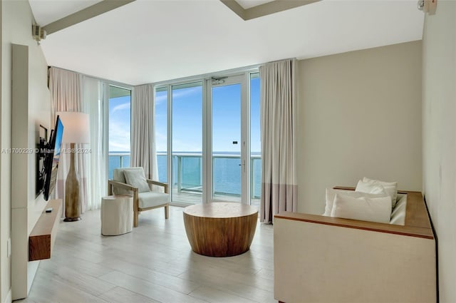 living area with light wood-type flooring, a water view, and floor to ceiling windows