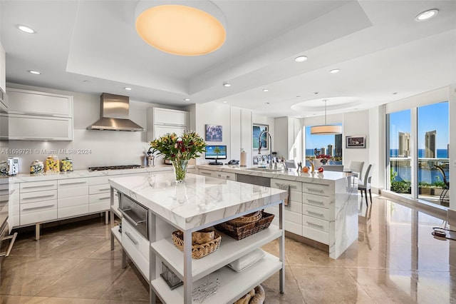 kitchen featuring wall chimney exhaust hood, a kitchen island, white cabinetry, and a tray ceiling