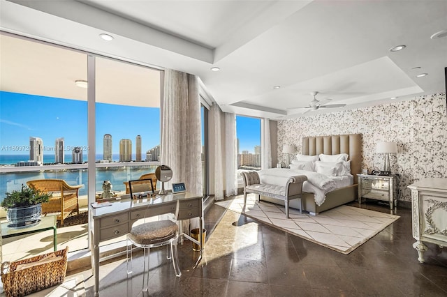 bedroom with a raised ceiling, ceiling fan, and a water view