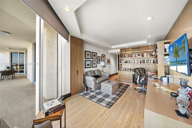 home office with a tray ceiling and light hardwood / wood-style flooring