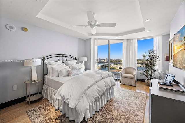 bedroom with a raised ceiling, ceiling fan, and light hardwood / wood-style floors