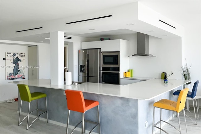 kitchen with white cabinets, appliances with stainless steel finishes, a kitchen breakfast bar, and wall chimney exhaust hood