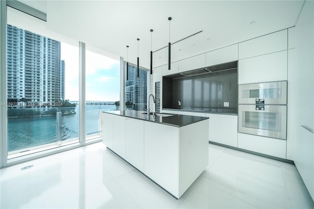 kitchen featuring sink, hanging light fixtures, white cabinets, an island with sink, and a water view