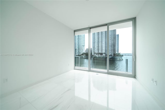 tiled spare room featuring a water view and a wall of windows