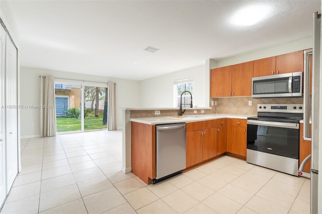 kitchen featuring backsplash, sink, light tile patterned floors, appliances with stainless steel finishes, and kitchen peninsula