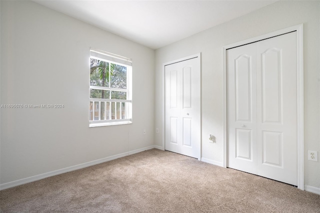 unfurnished bedroom featuring light colored carpet and multiple closets