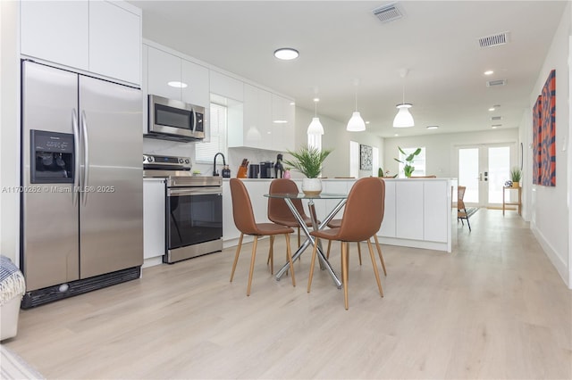 kitchen featuring appliances with stainless steel finishes, decorative light fixtures, white cabinetry, and light hardwood / wood-style flooring