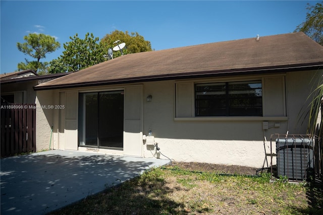 rear view of house featuring stucco siding, roof with shingles, central AC unit, and a patio area