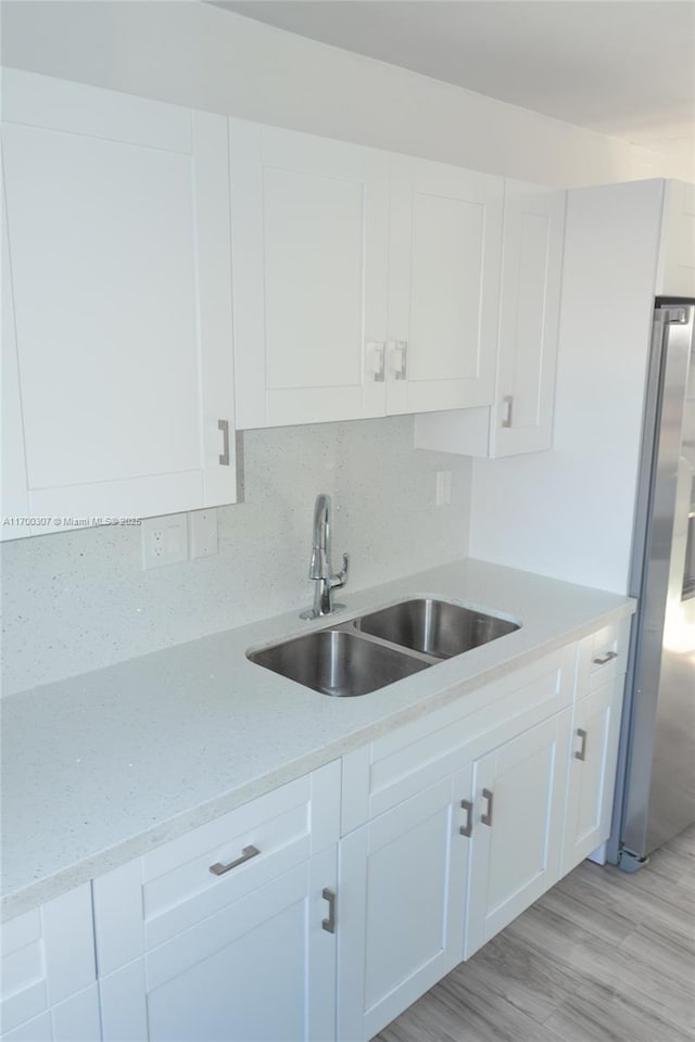 kitchen with white cabinets, light hardwood / wood-style floors, sink, stainless steel refrigerator, and light stone counters