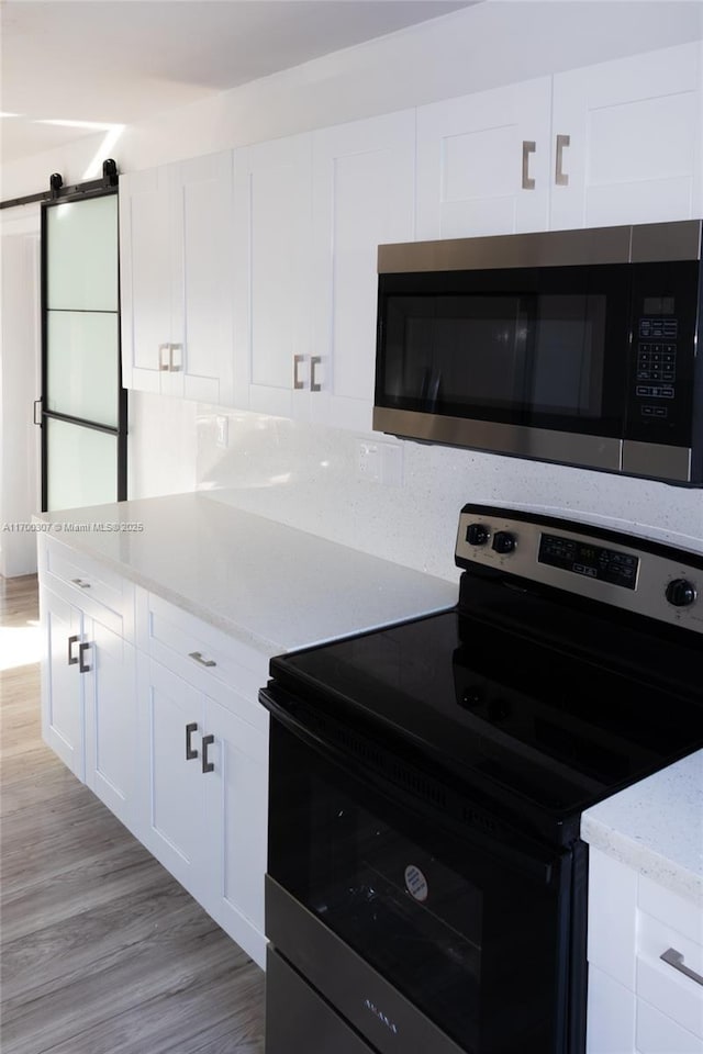 kitchen featuring a barn door, white cabinetry, light wood-type flooring, stainless steel appliances, and light stone counters