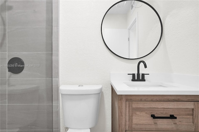 full bathroom with a textured wall, toilet, a stall shower, and vanity