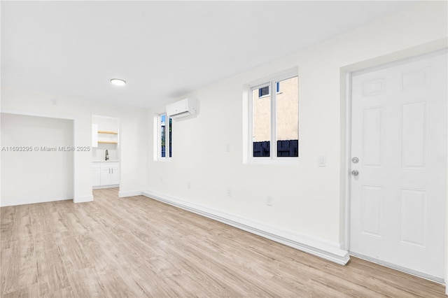 spare room with light wood-style flooring, an AC wall unit, and baseboards