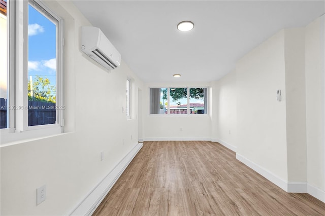 spare room featuring a wall mounted AC, plenty of natural light, baseboards, and light wood-type flooring