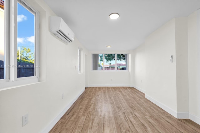 unfurnished room featuring light wood finished floors, baseboards, a wall mounted air conditioner, and a wealth of natural light