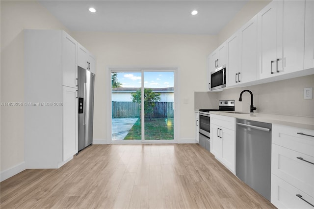 kitchen with light countertops, a sink, appliances with stainless steel finishes, light wood-style flooring, and white cabinets