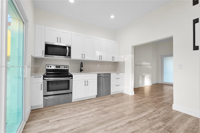 kitchen featuring white cabinets, light wood-style flooring, light countertops, appliances with stainless steel finishes, and a sink