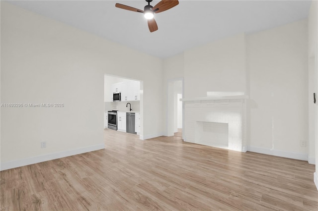 unfurnished living room with a ceiling fan, a sink, baseboards, and light wood-type flooring