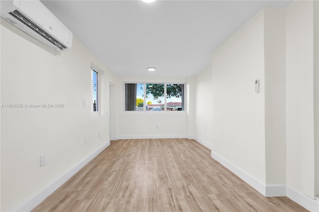 spare room featuring a wall mounted AC, baseboards, and light wood-type flooring