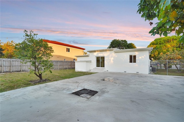 back of property at dusk featuring stucco siding, a fenced backyard, a yard, and a patio area