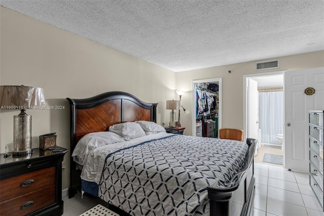 bedroom featuring a walk in closet, a closet, light tile patterned floors, and a textured ceiling