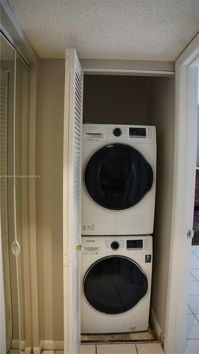 laundry room featuring light tile patterned floors, stacked washing maching and dryer, and a textured ceiling