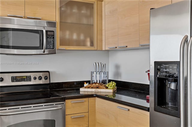 kitchen with dark stone counters, light brown cabinets, and stainless steel appliances