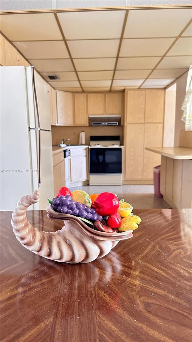 kitchen featuring a drop ceiling, light brown cabinets, white appliances, and range hood