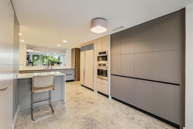 kitchen with a kitchen bar, gray cabinetry, paneled fridge, stainless steel double oven, and sink