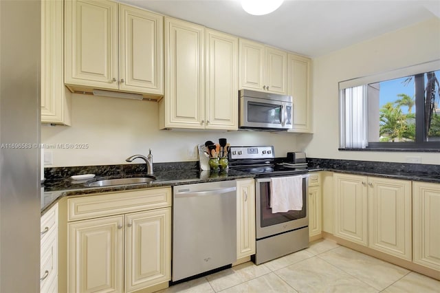 kitchen featuring cream cabinets, dark stone counters, appliances with stainless steel finishes, light tile patterned flooring, and sink