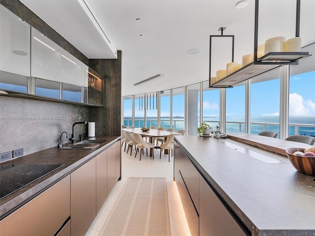 kitchen with dark countertops, tasteful backsplash, a sink, a water view, and black electric stovetop