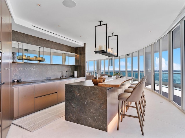 kitchen with decorative backsplash, sink, a water view, light tile patterned floors, and expansive windows