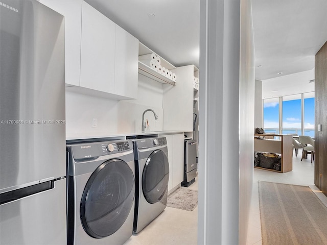 laundry room with cabinet space, a water view, a sink, and separate washer and dryer
