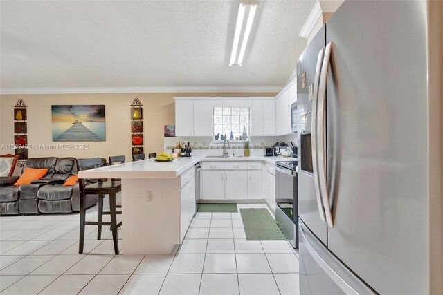 kitchen featuring white cabinets, crown molding, appliances with stainless steel finishes, a kitchen bar, and kitchen peninsula