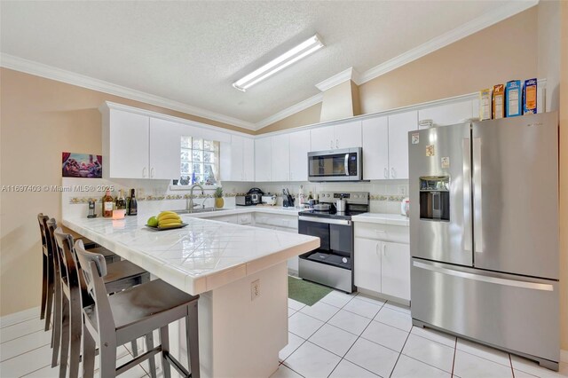 kitchen featuring kitchen peninsula, appliances with stainless steel finishes, vaulted ceiling, and white cabinetry