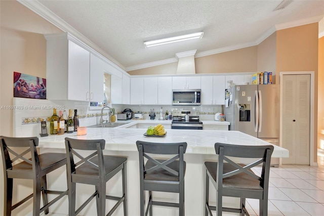 699 NW 134th Pl, Miami, FL 33182 - kitchen with appliances with stainless steel finishes, white cabinetry, vaulted ceiling, a sink, and a peninsula