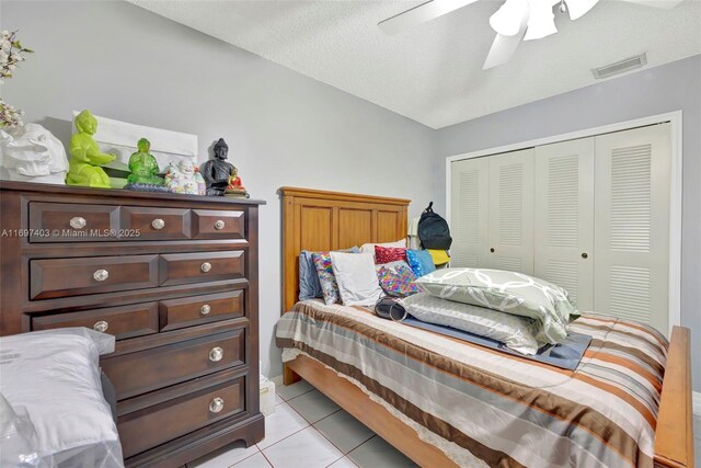 bedroom with ceiling fan, a closet, light tile patterned floors, and a textured ceiling